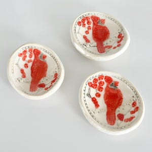 May include: Three small white ceramic bowls with red cardinal bird designs. Each bowl features a cardinal bird perched on a branch with red berries.