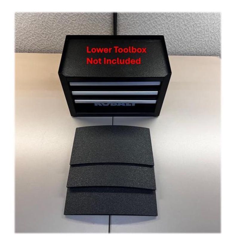 May include: A black metal toolbox with three drawers and silver handles. The text "Lower Toolbox Not Included" is printed in red on the top. Three black textured rectangular drawer liners are positioned in front of the toolbox unit.