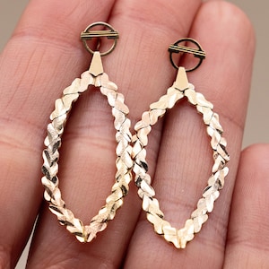 Puede incluir: Un par de pendientes ovalados abiertos en tono dorado. Cada pendiente presenta un diseño texturizado y tejido dentro de la forma ovalada. Los pendientes tienen una pequeña parte superior circular con una barra decorativa.