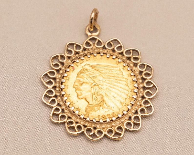May include: A gold pendant with a coin depicting an Indian head profile, encased in a decorative filigree frame. The pendant includes a loop for a chain and is a vintage item. The coin is dated 1928.