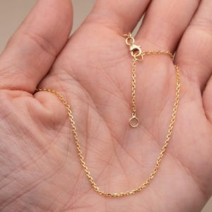 May include: A delicate gold-coloured chain necklace with a lobster clasp and adjustable length. The chain is made of small, evenly spaced links. The necklace is displayed on a neutral background.
