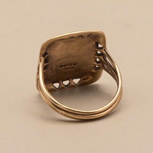 May include: A vintage gold ring with a rectangular face and a detailed band. The ring's face has a textured surface with small, decorative cutouts along the edges. The band features a double-layered design, adding to its classic appeal.