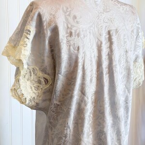 May include: A light gray satin nightgown featuring a tonal paisley jacquard pattern throughout. The garment has short sleeves finished with cream-colored lace trim and a matching lace detail along the neckline, providing a soft texture.