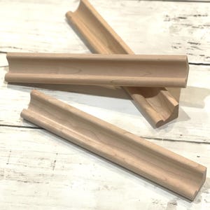 May include: Three pieces of unfinished, natural wood trim with a rounded, curved edge. The trim is designed to be used as a decorative molding for furniture or home decor.