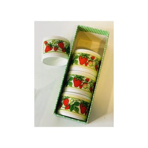 May include: Set of six white ceramic napkin rings with a strawberry design. The rings are stacked in a green and white checkered box.