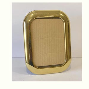 May include: A rectangular, gold-colored picture frame with rounded corners. The frame has a shiny, metallic finish and a cardboard backing. The frame is designed to hold a photograph or artwork and is suitable for tabletop display.