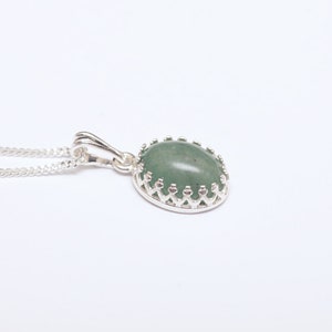 Puede incluir: Un collar con colgante de plata con una piedra preciosa ovalada de color verde claro. La piedra preciosa est&aacute; engastada en un bisel decorativo de plata. La cadena del collar es una delicada cadena de plata.