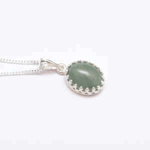 Puede incluir: Collar de plata con colgante. El colgante tiene una piedra preciosa ovalada de color verde claro engastada en un bisel decorativo de plata. La cadena del collar es una fina cadena de plata.