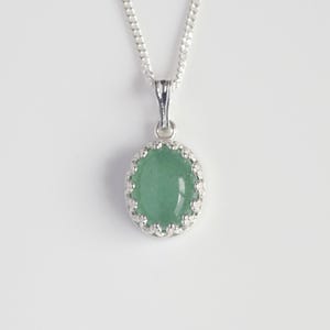 Puede incluir: Un collar de plata con un colgante redondo con una piedra preciosa verde claro. La piedra preciosa est&aacute; engastada en un marco de plata decorativo y festoneado. La cadena es de dise&ntilde;o delicado y enlazado.