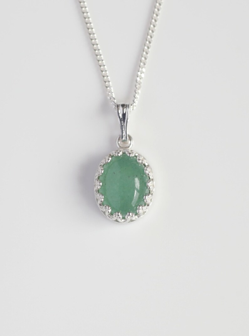 Puede incluir: Un collar de plata con un colgante redondo con una piedra preciosa verde claro. La piedra preciosa est&aacute; engastada en un marco de plata decorativo y festoneado. La cadena es de dise&ntilde;o delicado y enlazado.