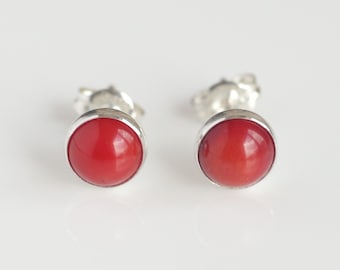 May include: A pair of silver stud earrings with round red coral stones.