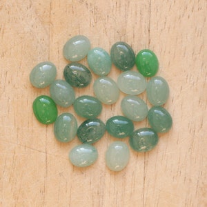 Puede incluir: Una colecci&oacute;n de piedras preciosas ovaladas en varios tonos de verde, desde menta claro hasta verde bosque profundo. Las piedras pulidas est&aacute;n dispuestas sobre una superficie de madera clara, mostrando su textura suave y brillante y sus variaciones naturales.