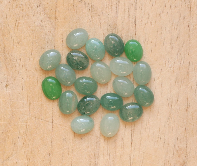 Puede incluir: Una colecci&oacute;n de piedras preciosas ovaladas en varios tonos de verde, desde menta claro hasta verde bosque profundo. Las piedras pulidas est&aacute;n dispuestas sobre una superficie de madera clara, mostrando su textura suave y brillante y sus variaciones naturales.