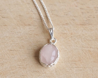 May include: A delicate silver chain necklace with a pink rose quartz pendant. The pendant is oval-shaped and set in a silver filigree frame.