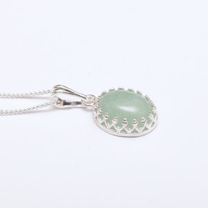 Puede incluir: Un collar con colgante de plata con una piedra preciosa ovalada de color verde claro. La piedra preciosa est&aacute; engastada en un bisel decorativo de plata con un dise&ntilde;o de corona. La cadena del collar tambi&eacute;n es de plata.