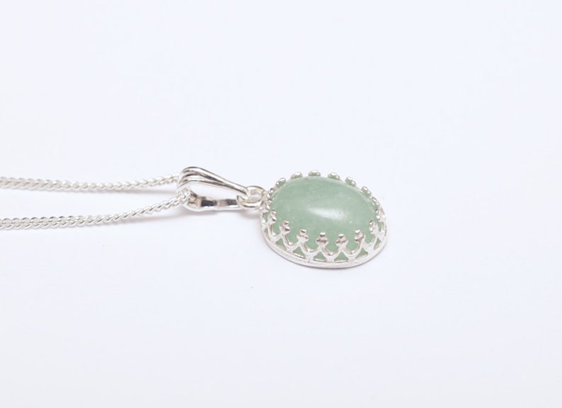 Puede incluir: Un collar con colgante de plata con una piedra preciosa ovalada de color verde claro. La piedra preciosa est&aacute; engastada en un bisel decorativo de plata con un dise&ntilde;o de corona. La cadena del collar tambi&eacute;n es de plata.