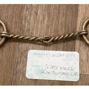 May include: A horse bit with a twisted central section and two large circular rings. The bit is made of a brass-coloured metal. The tag reads "5.25" Never Rust Twisted LR."