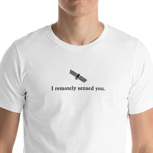 May include: White t-shirt with a black graphic of a satellite and the text "I remotely sensed you." The shirt is made of a soft material and has short sleeves.