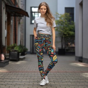 May include: Black leggings with a colourful pattern of words and phrases related to technology and coding. The leggings are being worn by a person standing on a pavement.