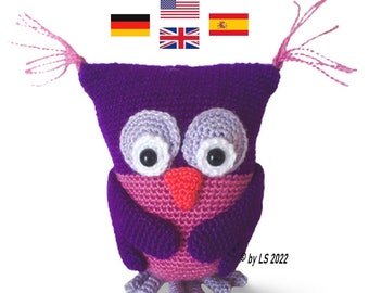 May include: A purple crocheted owl with pink accents, including the beak, feet, and tufts of feathers on the head. The owl has large, black eyes with white pupils. The owl is standing on a white background. The image also includes four flags: German, American, British, and Spanish.