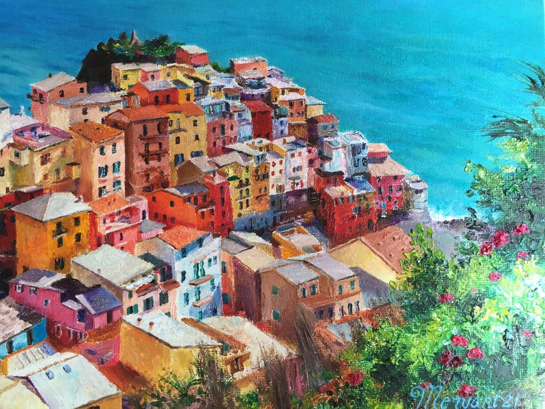 May include: A colourful painting of a hillside village overlooking a turquoise ocean. The houses are painted in shades of yellow, orange, red, pink, and blue. Lush green foliage is in the foreground.