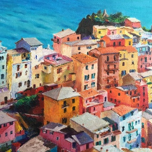May include: A colourful painting of a seaside town with buildings in shades of yellow, orange, red, pink, and blue. The buildings are clustered together on a hillside overlooking a blue body of water.