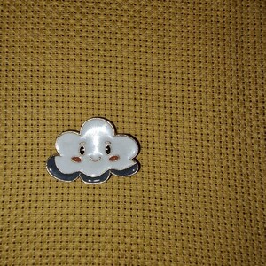 May include: A charming cloud-shaped enamel pin with a smiling face. It has a white body, grey accents, and a gold outline. The pin is set against a textured, golden-brown background.