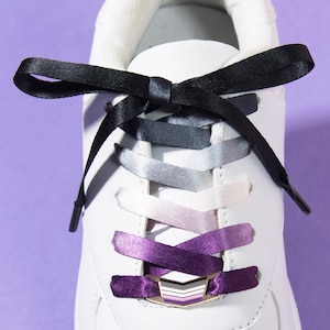 Puede incluir: Zapatilla blanca con cordones degradados en negro, gris, plateado, lavanda y morado. Los cordones se aseguran con un cierre de cordones a juego. El texto "MATCHING LACE LOCK + SHOELACE SET" está en la parte inferior.