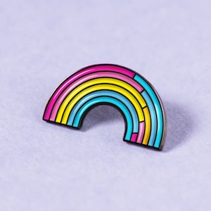 Pode incluir: Um broche de esmalte em forma de arco-íris. O broche é feito de listras rosa, amarelas, azuis e verdes.