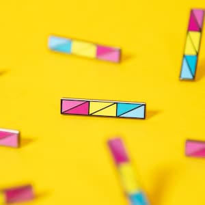 Pode incluir: Uma coleção de broches de esmalte coloridos com designs geométricos em tons de rosa, azul e amarelo. Os broches estão espalhados sobre um fundo amarelo brilhante.