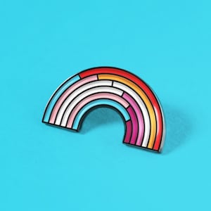 May include: A rainbow-colored enamel pin in the shape of an arc. The pin has a black outline and is made up of stripes of red, orange, yellow, white, light blue, pink, and purple.