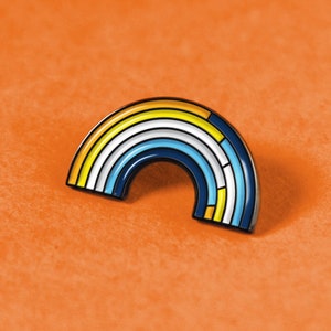 May include: A rainbow-colored enamel pin in the shape of an arc. The pin has a blue outline and is filled with yellow, white, and blue stripes.