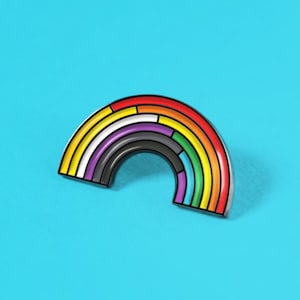 May include: A colorful rainbow pin with a variety of colors, including red, orange, yellow, green, blue, purple, black, and white. The pin is set against a bright blue background. The pin is a half-circle shape.