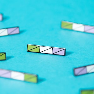 May include: A collection of 10 small, rectangular pins with a geometric design. The pins are a mix of green, white, and purple colors. The pins are arranged in a scattered pattern on a bright blue background.