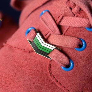 May include: Close-up of a pair of red suede shoes with blue shoelaces and a green, white, and black pin on the right shoe.