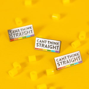 May include: Three enamel pins on a yellow background. Each pin features the text "Can't Think Straight" in black with a rainbow stripe underneath.
