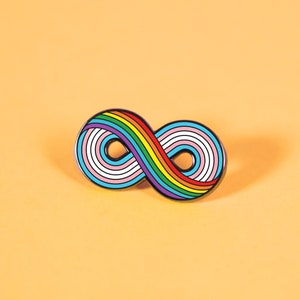 May include: A rainbow infinity symbol pin with a white and light blue stripe in the center. The pin is on a light orange background.