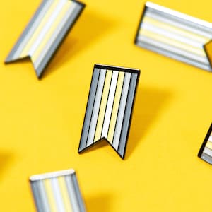 May include: A collection of ten small, colorful enamel pins in the shape of flags. The pins have a black outline and are decorated with alternating yellow and white stripes.