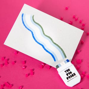 May include: A white card with a colorful wavy design, with a white rectangular object with the text "THE PIN PRICK" and a social media handle. The background is a bright pink with small pink geometric shapes scattered around the card and object.