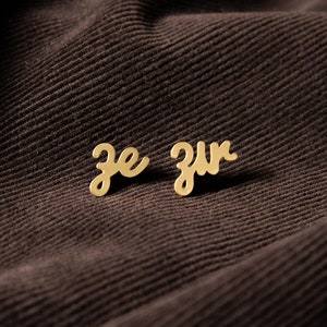 May include: Gold-colored earrings with the words "je zur" written in cursive.
