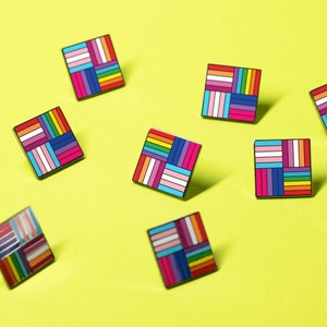 May include: Ten colorful square pins with a geometric pattern of stripes. The pins are arranged in a scattered pattern on a yellow background.