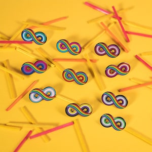 May include: Ten rainbow infinity symbol pins on a yellow background. The pins are arranged in a random pattern.