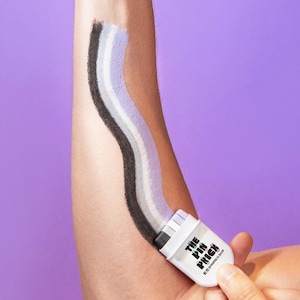 Pode incluir: Um braço com um gesto de polegar para cima, com um pincel aplicando um padrão ondulado de tinta preta, cinza e branca. A escova tem o texto "THE PIN PRICK". O fundo é roxo sólido.