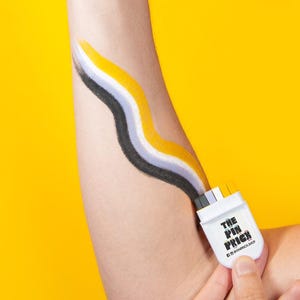 May include: A person's arm with a thumbs-up gesture, featuring a yellow background. The arm has a painted design of black, yellow, and gray wavy lines, connected to a white rectangular pin that reads "THE PIN PRICE".