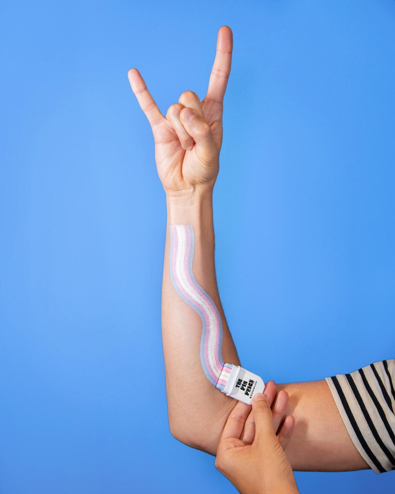 May include: A person's arm with a wavy, pastel-colored design applied with a white applicator. The applicator has the text "THE PIN PATCH" printed on it. The person is making a rock and roll hand gesture against a blue background.
