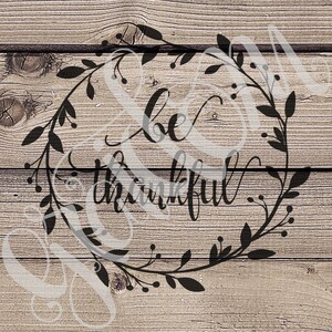 May include: A black and white graphic design on a wood background with a wreath of leaves and berries surrounding the words "be thankful".