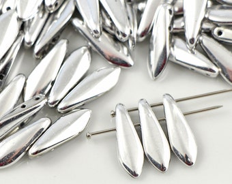 May include: A large pile of silver-colored glass beads in a teardrop shape. The beads are arranged in a random pattern and some are laying on a white surface. Three beads are strung on a silver wire.