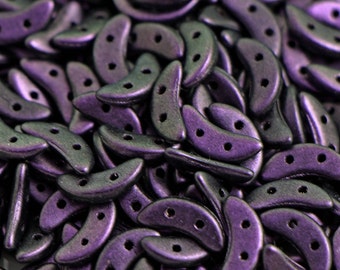 May include: A close-up of a pile of small, crescent-shaped beads. The beads are a dark purple color with a metallic sheen.