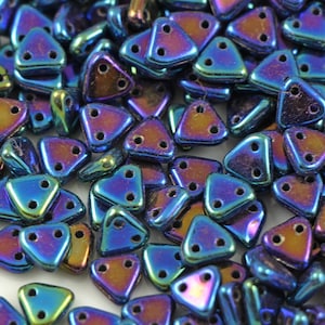 May include: A close-up of a pile of iridescent blue triangle-shaped beads with two holes each. The beads have a metallic sheen and are perfect for jewelry making.