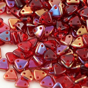 May include: A pile of red, iridescent triangle-shaped glass beads with two holes in each bead.